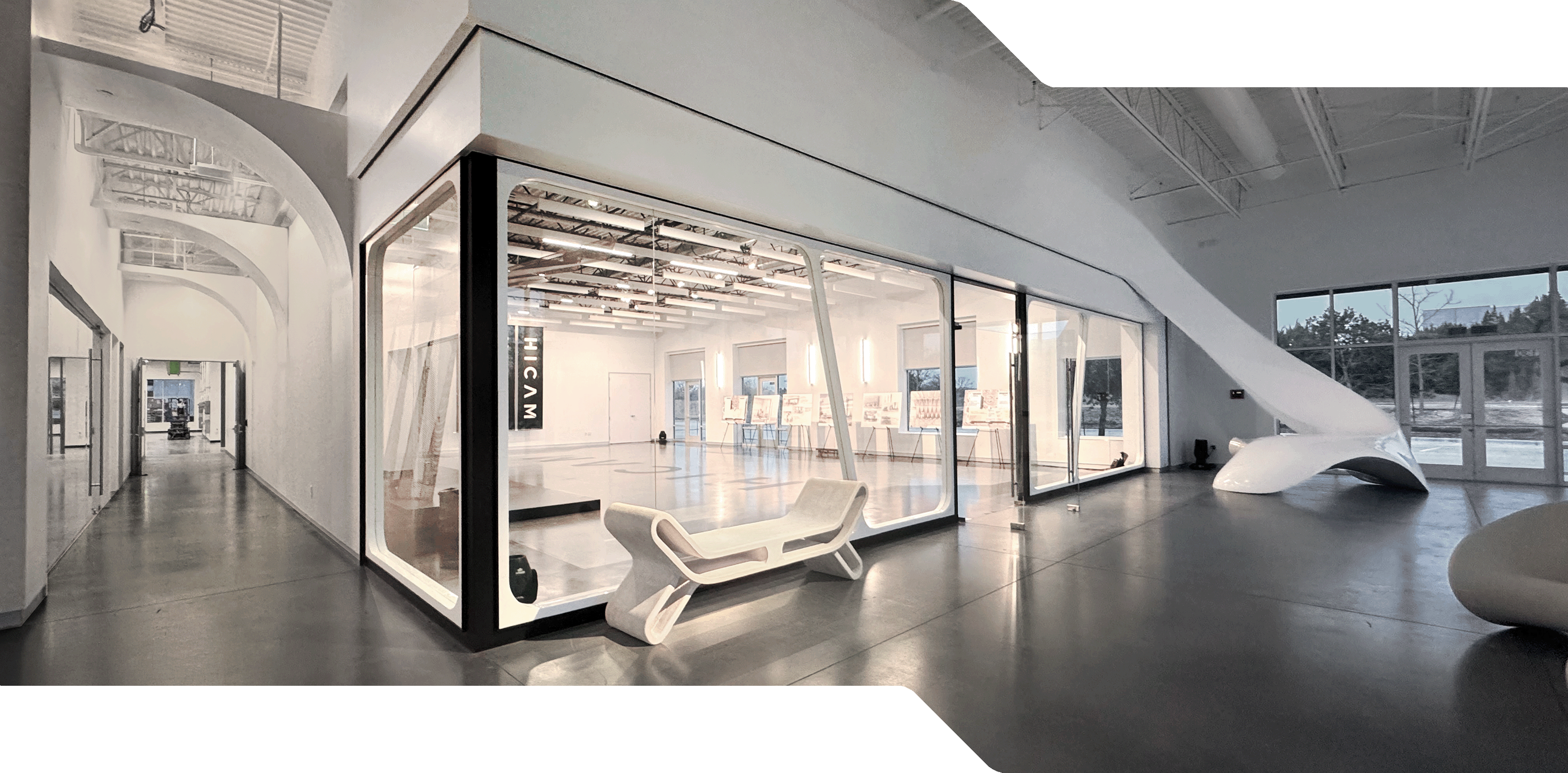 HICAM’s modern, spacious lobby with high ceilings, polished concrete floors, and sleek white architectural features. A large glass-walled event space room is centrally positioned, surrounded by sculptural furniture and natural light from large windows.