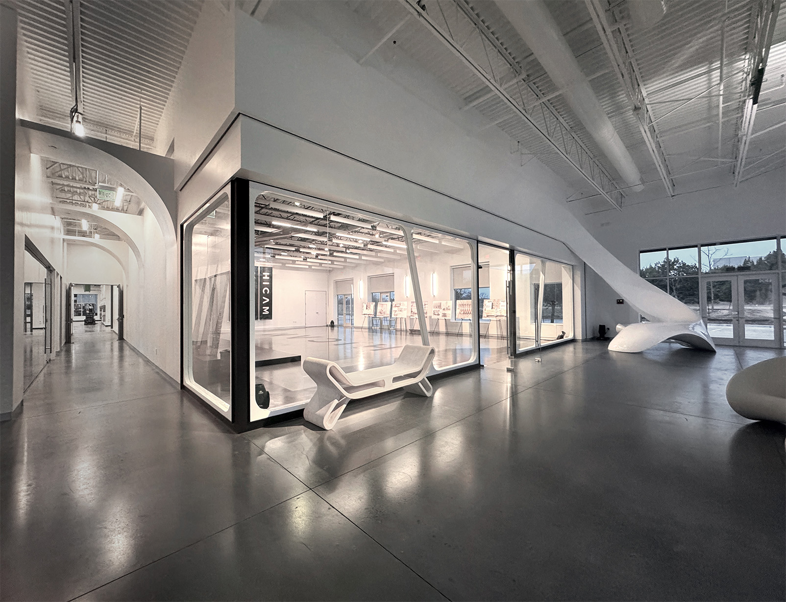 HICAM’s modern, spacious lobby with high ceilings, polished concrete floors, and sleek white architectural features. A large glass-walled event space room is centrally positioned, surrounded by sculptural furniture and natural light from large windows.